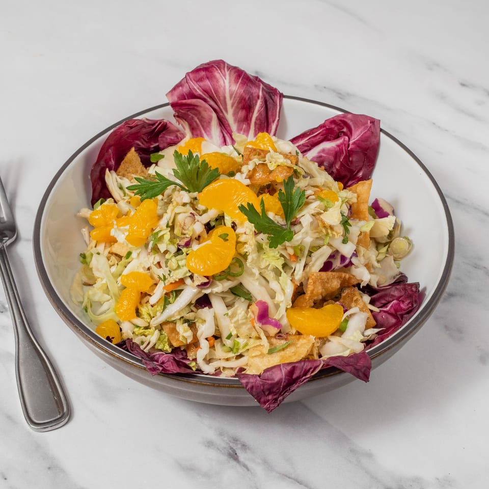 A vibrant salad with mandarin oranges, cabbage, wonton strips, and parsley in a bowl with a fork.