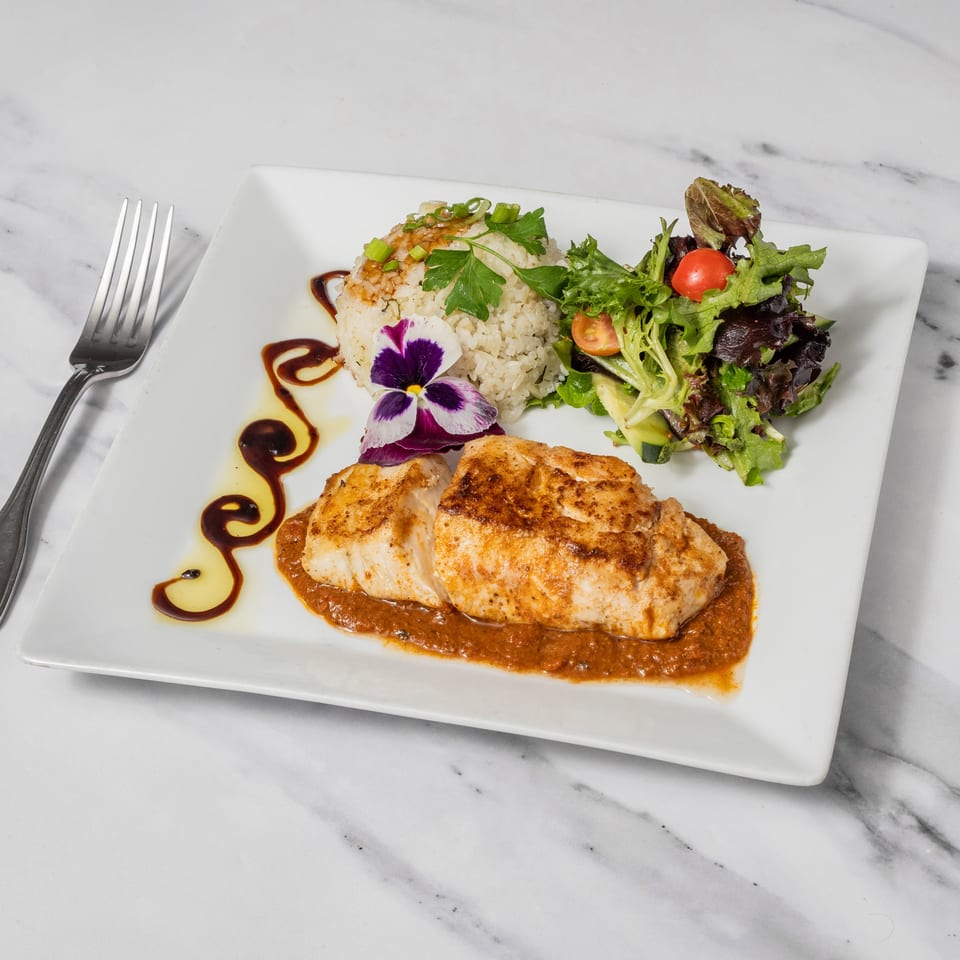 Pan-seared fish with rice, salad, and a purple edible flower on a white plate.